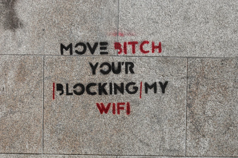 graffiti spray painted onto a grey wall reading move bitch, your blocking my wife