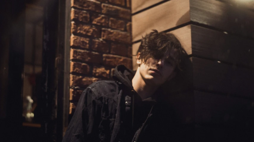 a young man is looking at his cellphone while he stands next to a brick building