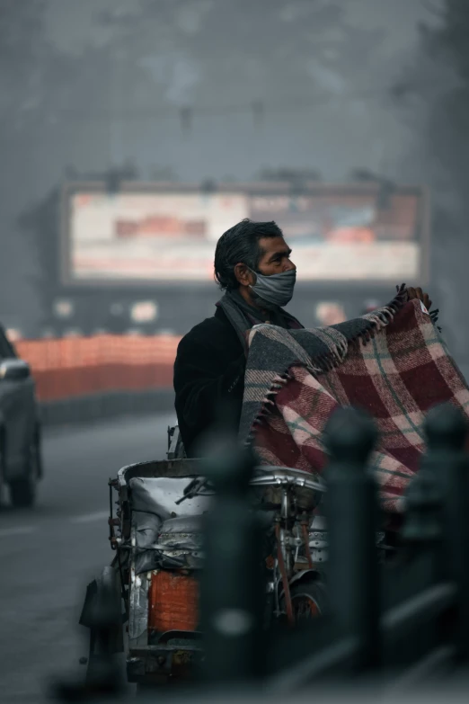 man in face mask riding bike with checkered blanket