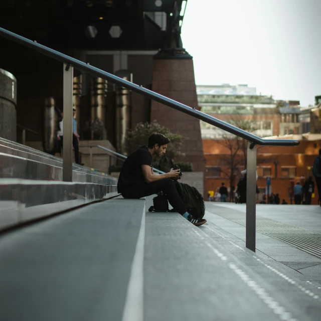 a young man sitting on the side of a long bench while texting on his phone