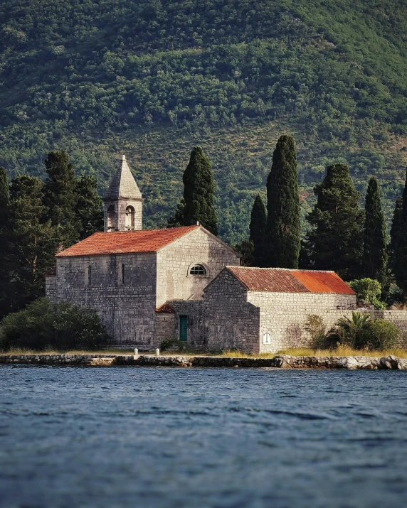 an old stone church next to a lake with trees around it