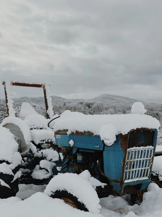 an old tractor covered in snow near a fence