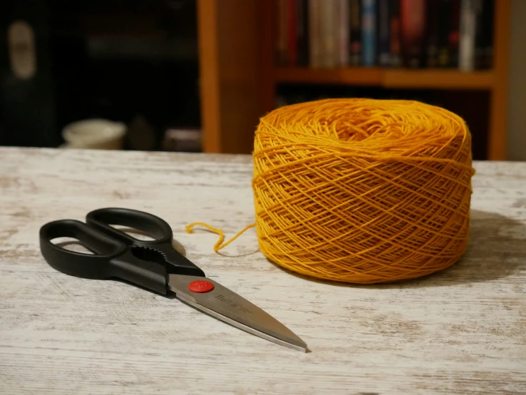 an orange ball of string next to scissors and yarn