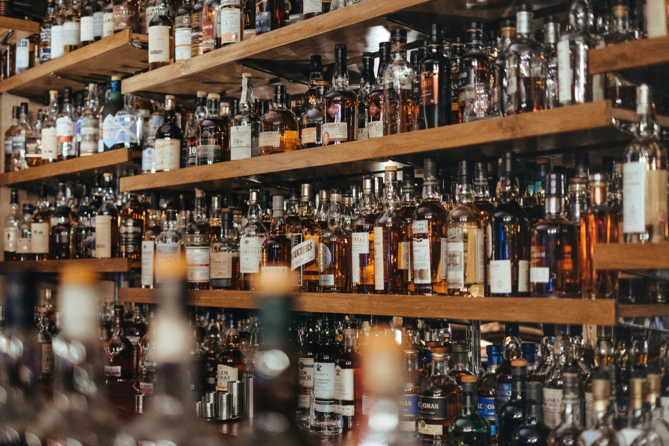 many bottles on shelves on one side, with blurry lights at the top