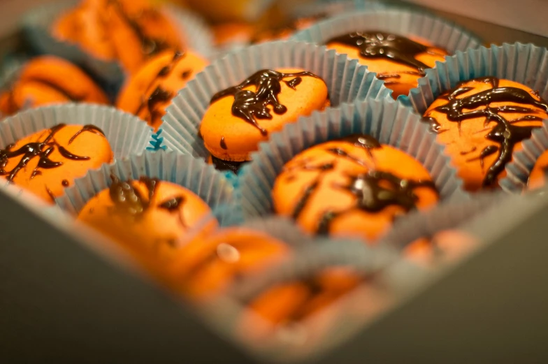 a box of yellow cupcakes with chocolate drizzled on them