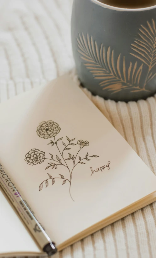 a drawing of flowers on an open notebook next to a mug