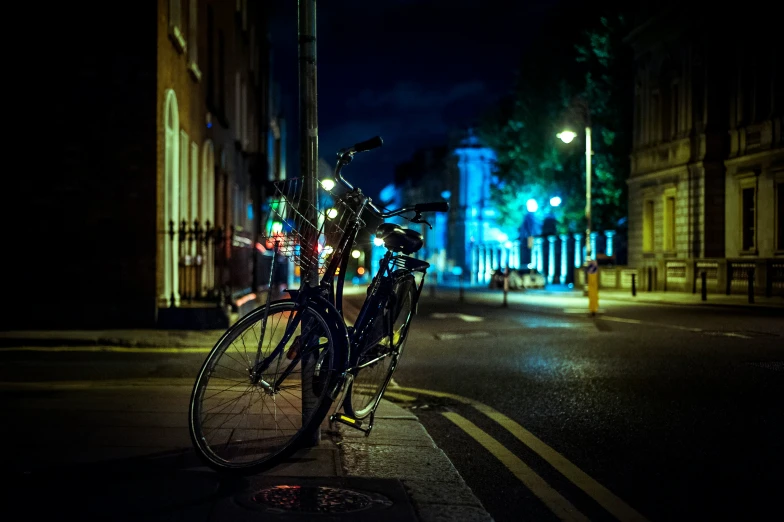 a bike leans against a post near an empty street at night