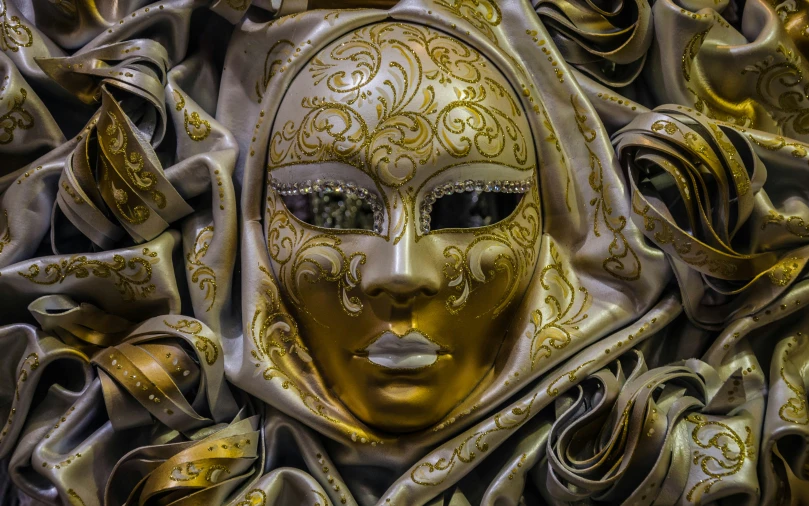 a golden mask surrounded by silver ribboned fabric