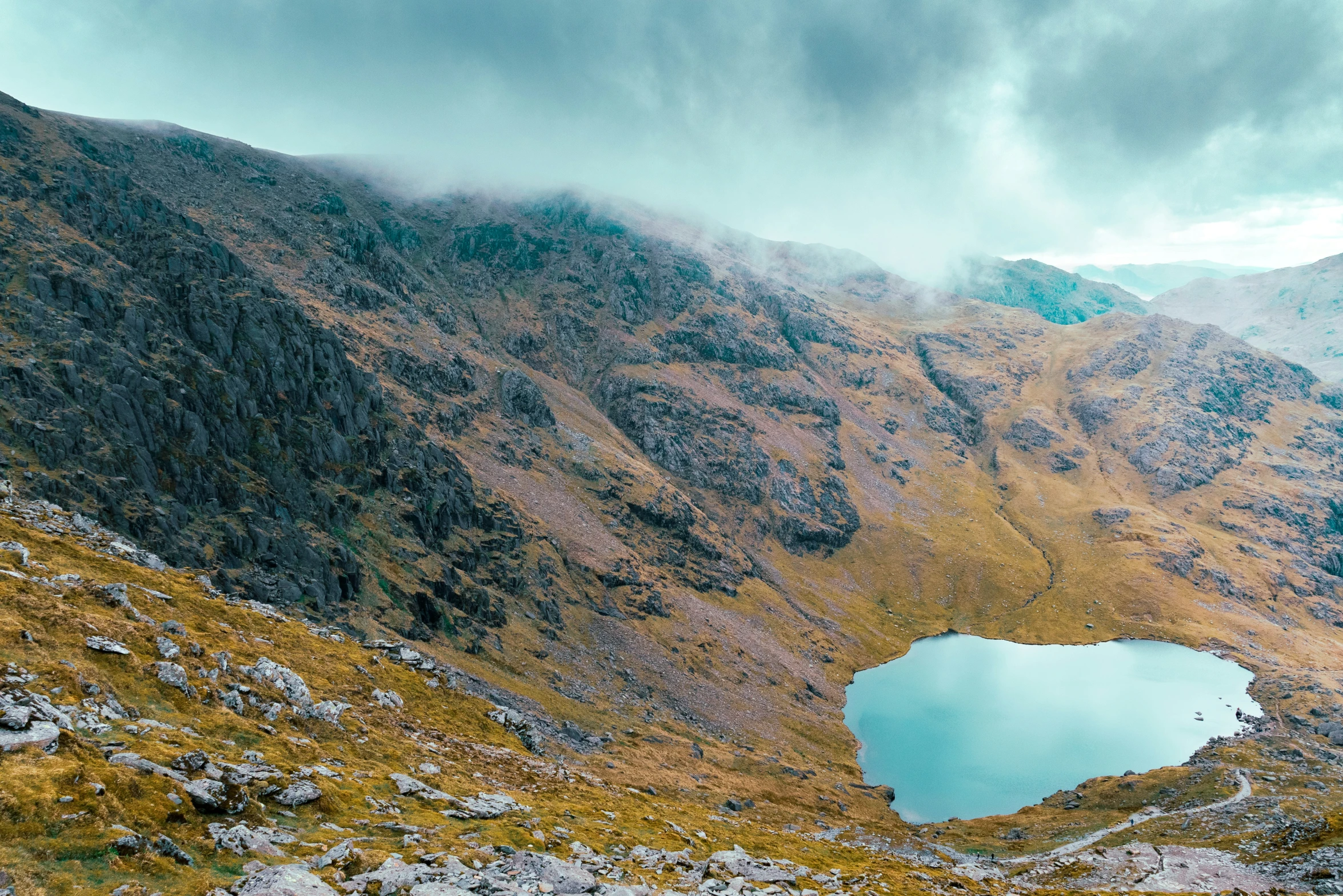 a view of the side of a mountain with a lake surrounded by mountains