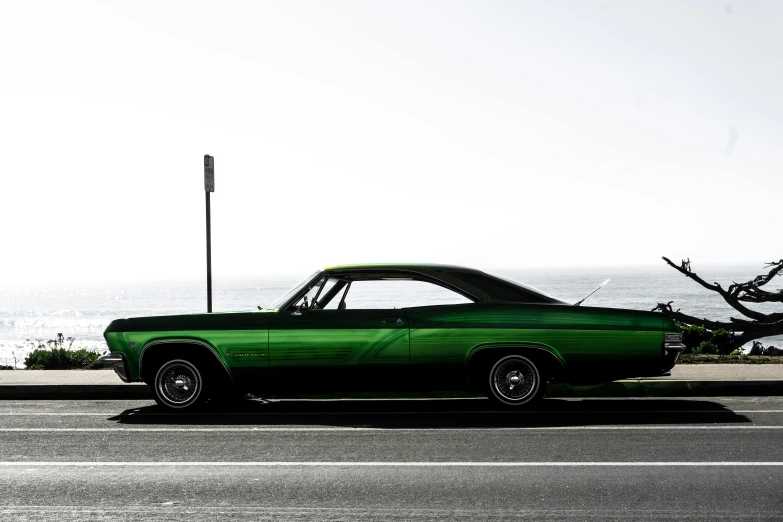 a green car sitting next to the ocean in front of a building