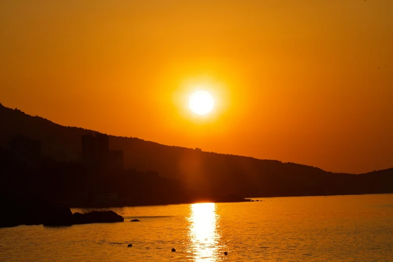 the sun is shining over a lake with hills on the horizon