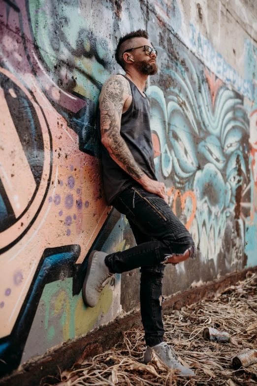 a man leaning on a graffiti wall with a skateboard