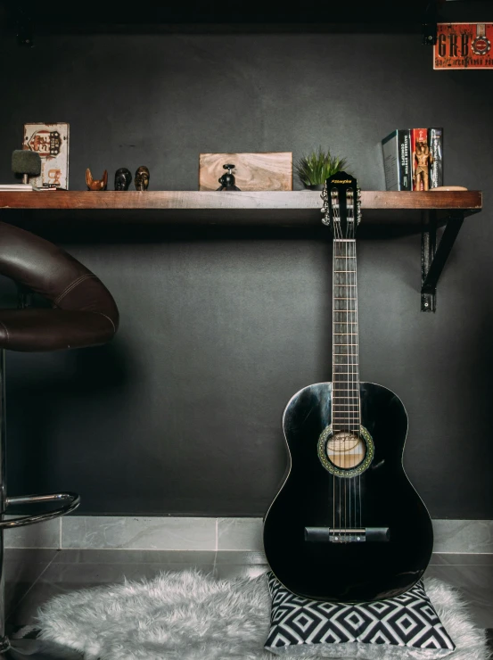 a guitar and a book shelf are seen against a gray wall