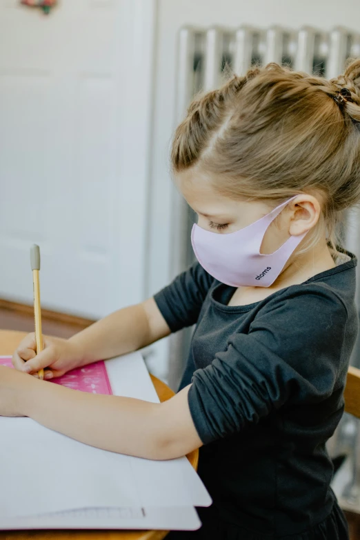 a child in a mask is writing on a piece of paper