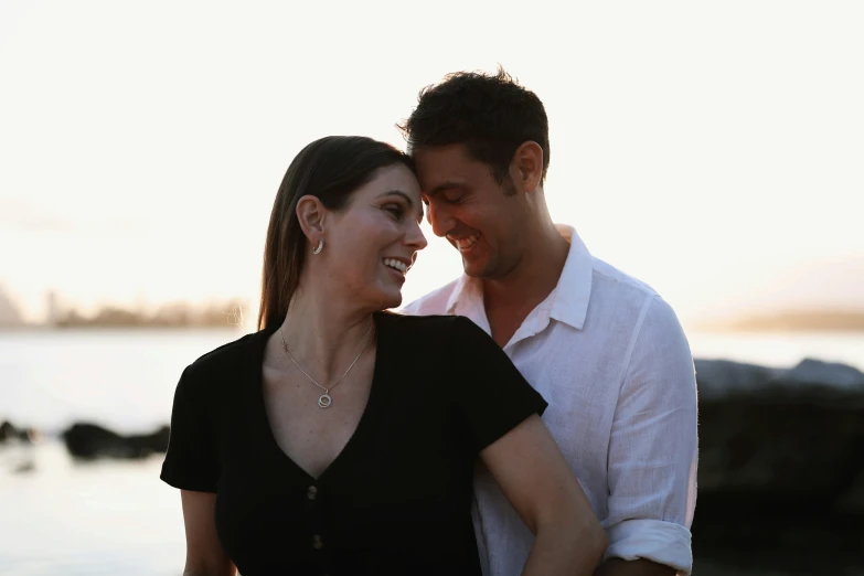 a smiling couple cuddling at the beach near the water