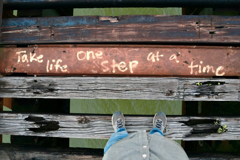 someones feet on a wooden bench near a sign