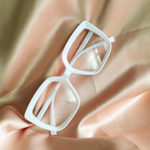 a white pair of glasses sitting on a satin surface