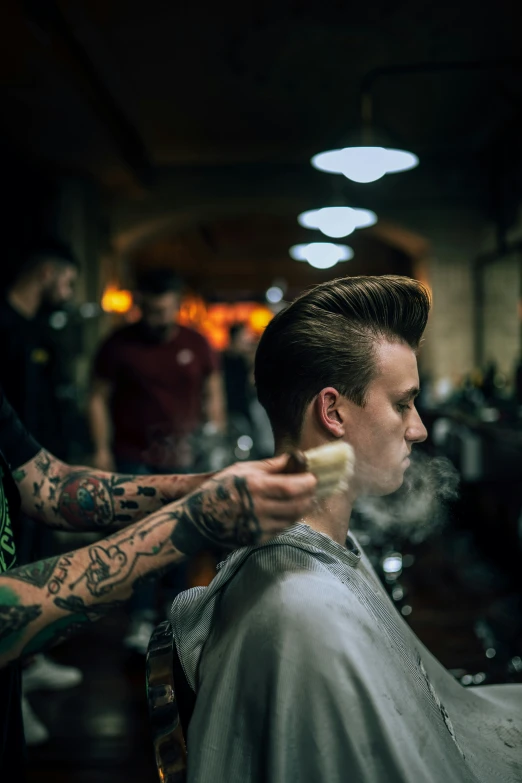 a barber shaving the mans hair in a room filled with other people
