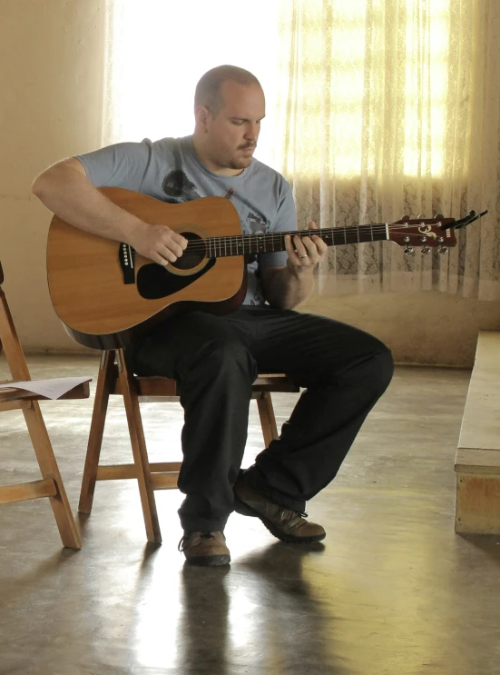 a man sitting on top of a chair while playing an acoustic guitar