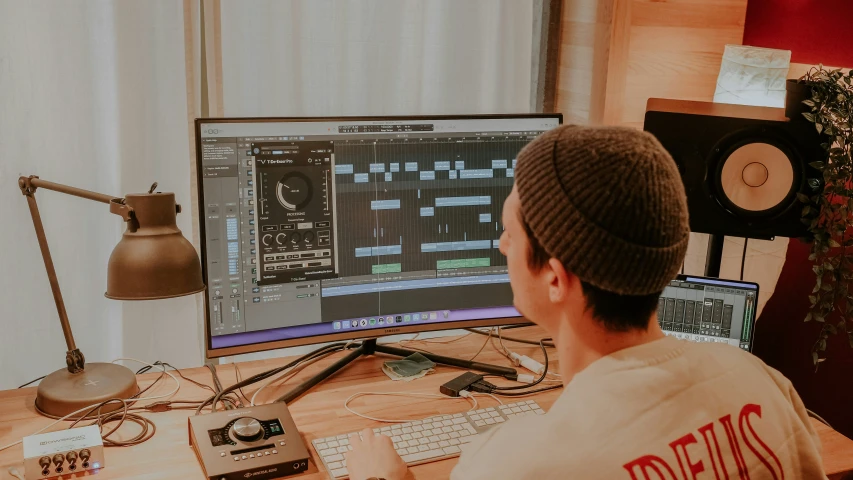 a man in front of a computer, looking at the sound mixer on the computer screen