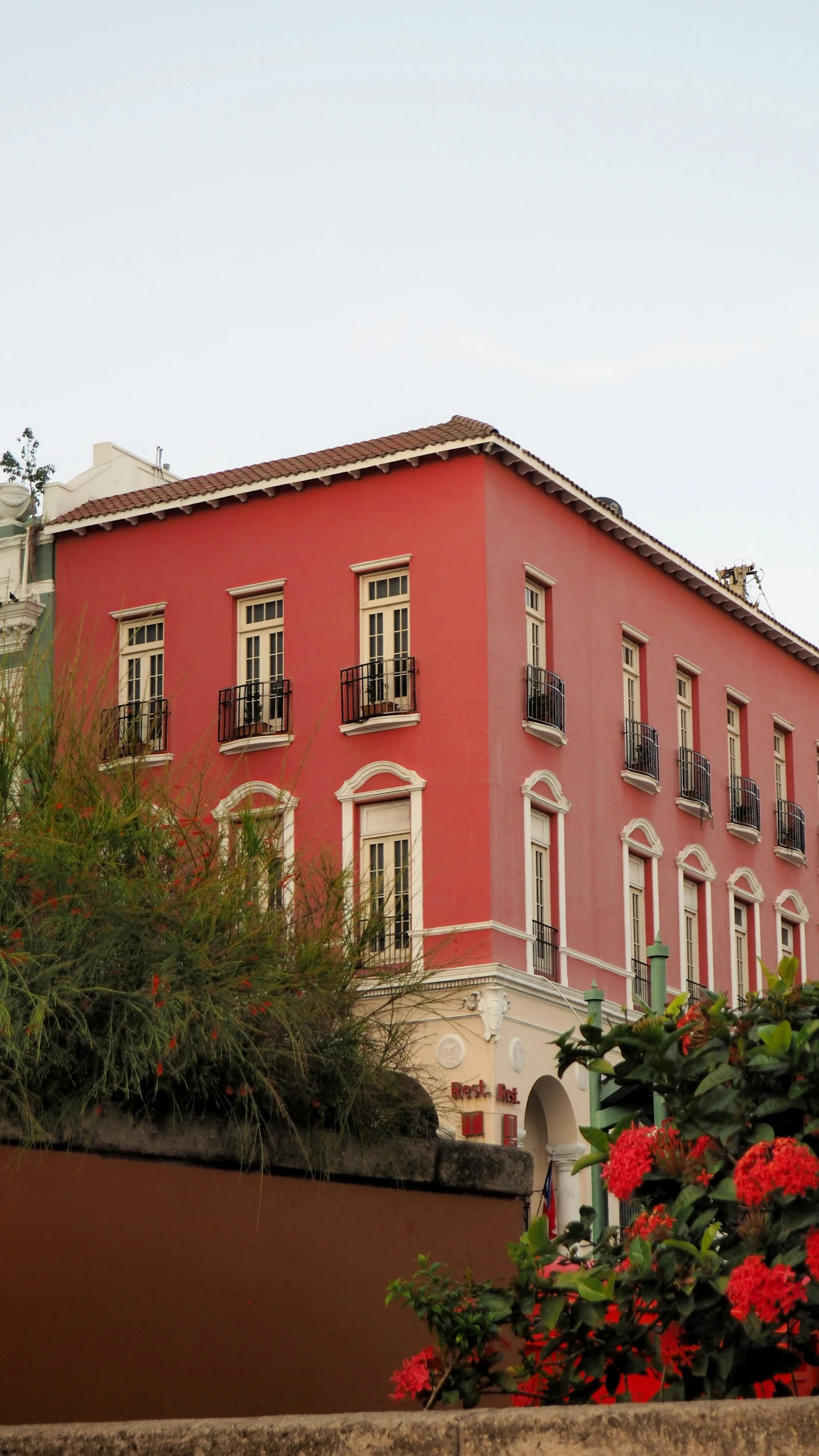 an old building is painted pink and surrounded by plants