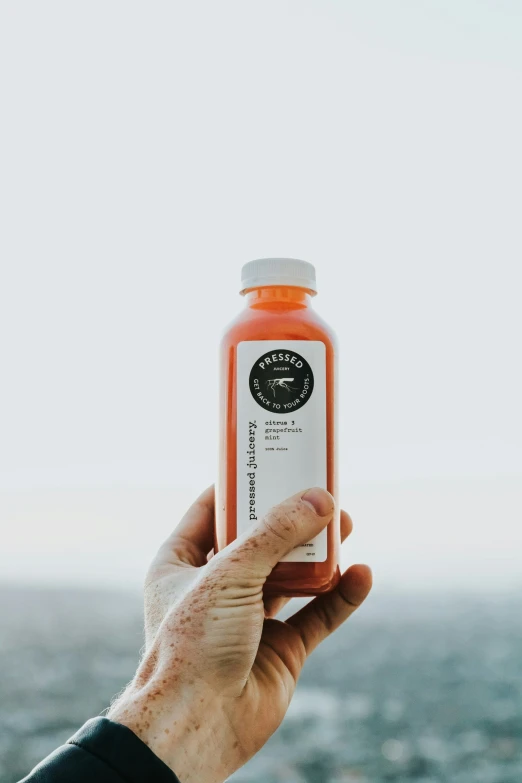 a person is holding up an orange juice in front of a sky background