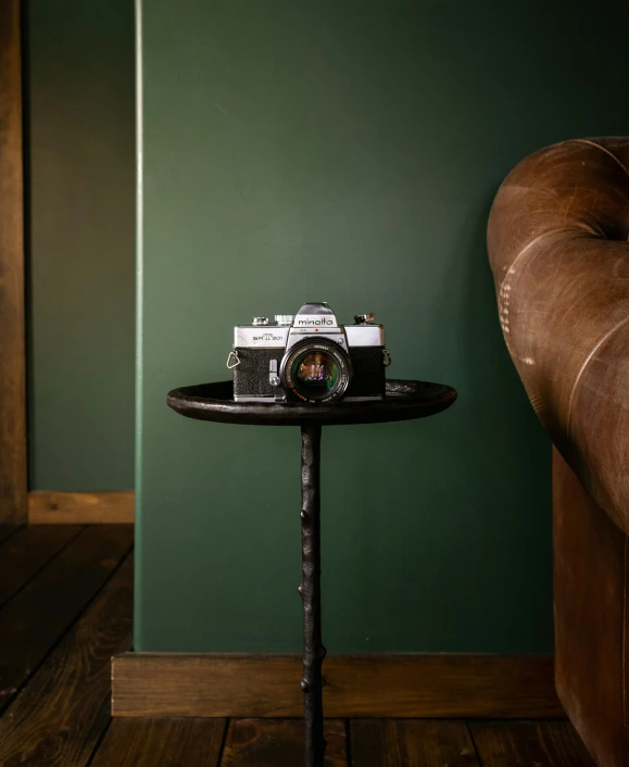 small table holding a brown leather chair and an old fashioned camera