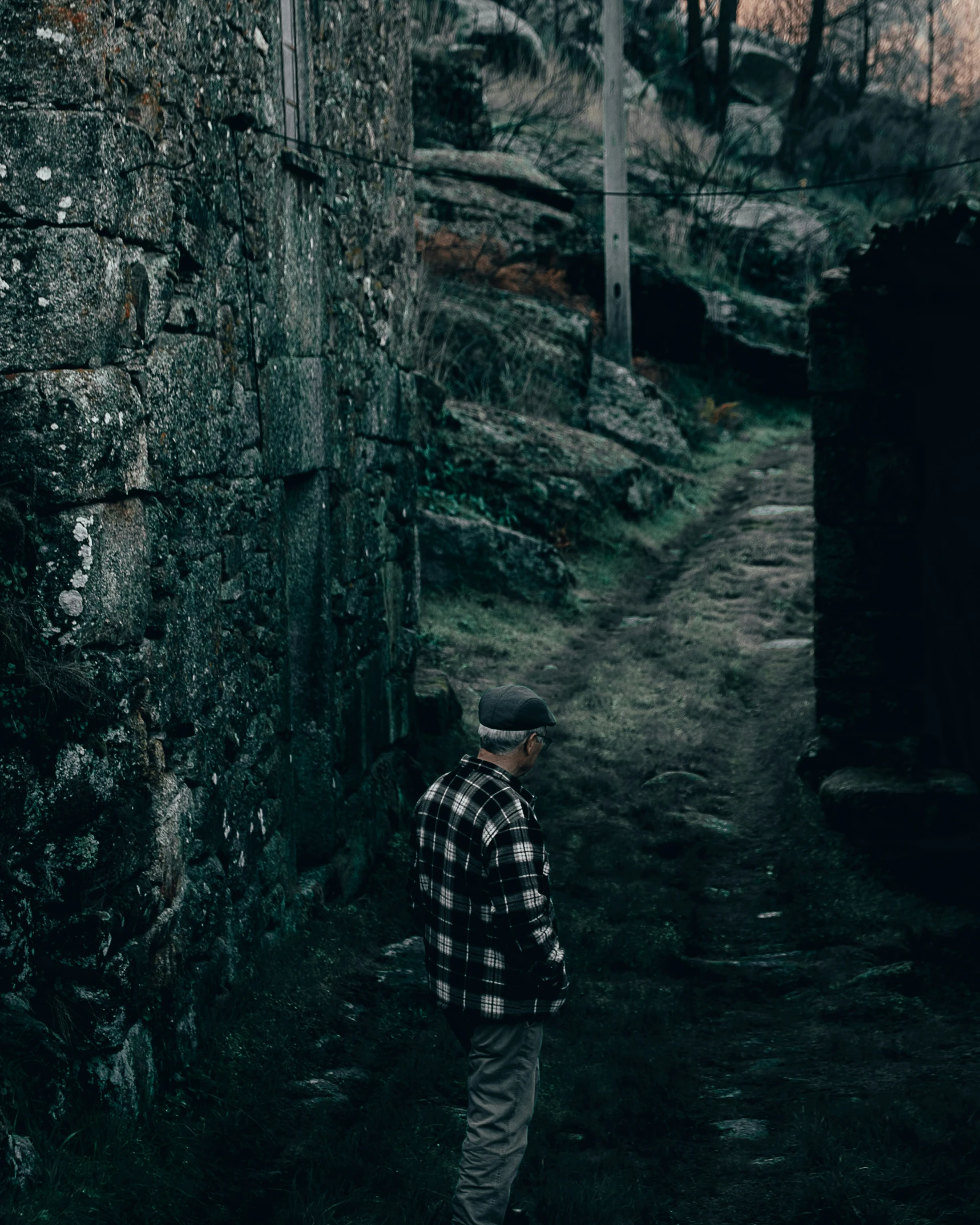 a man standing on the side of a dirt road next to a stone wall