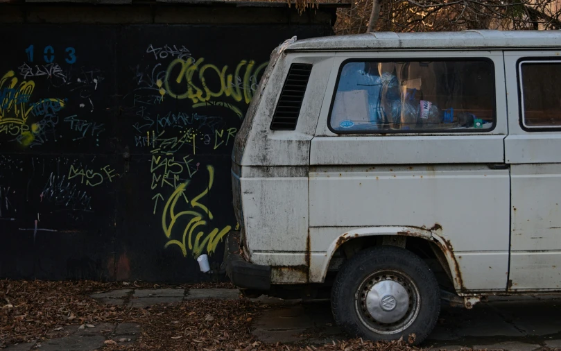 an old van is parked next to a wall that has spray painted graffiti