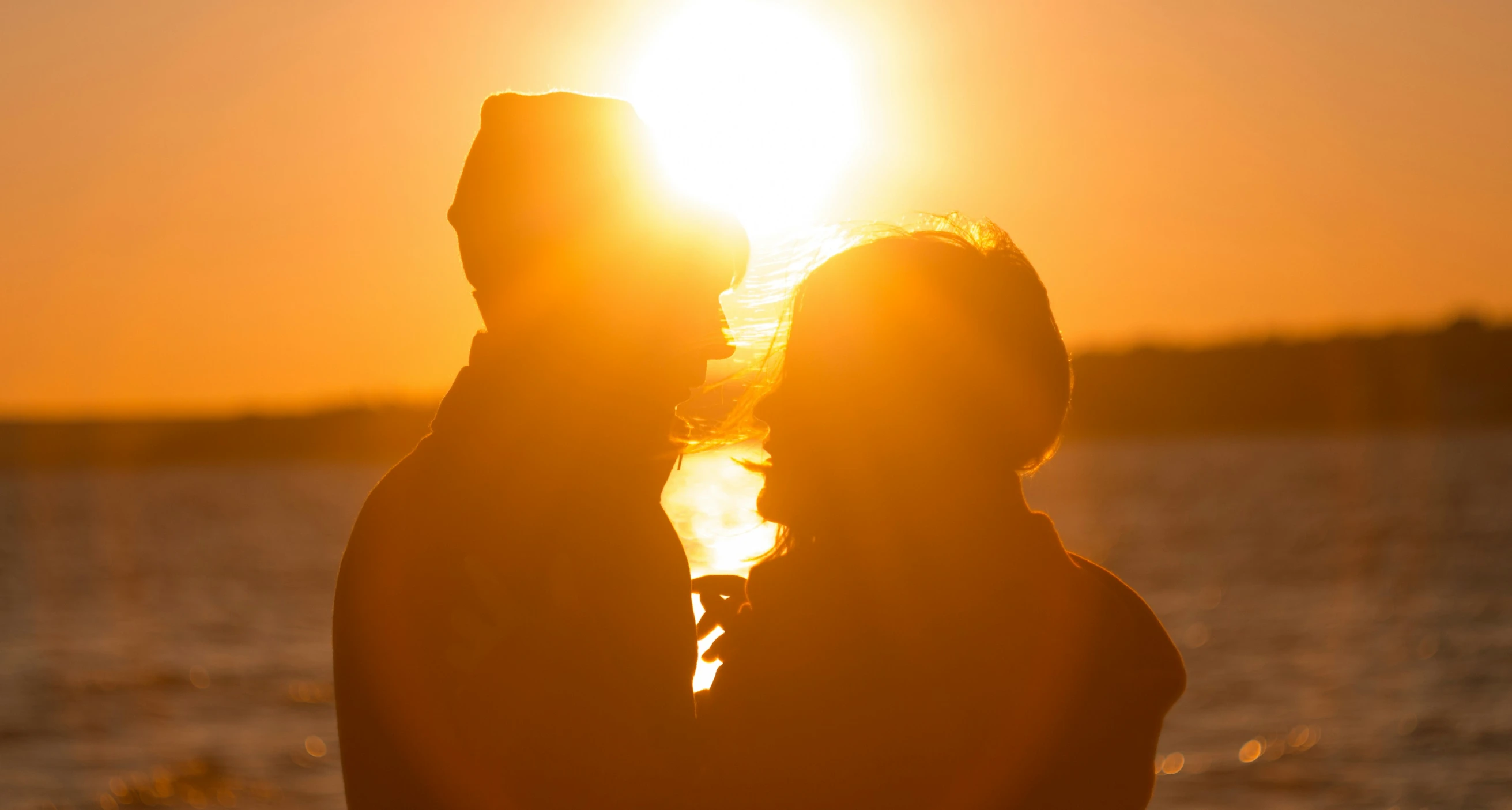 two people standing by water at sunset touching the head of each other