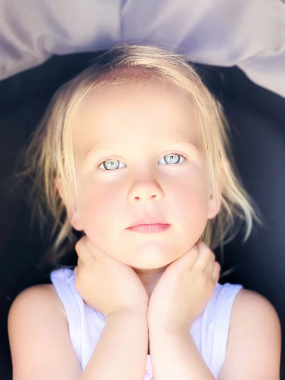 a small child with blue eyes sits under a blanket