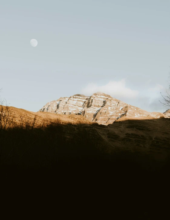 the moon rises behind the mountain with the grass on the hill