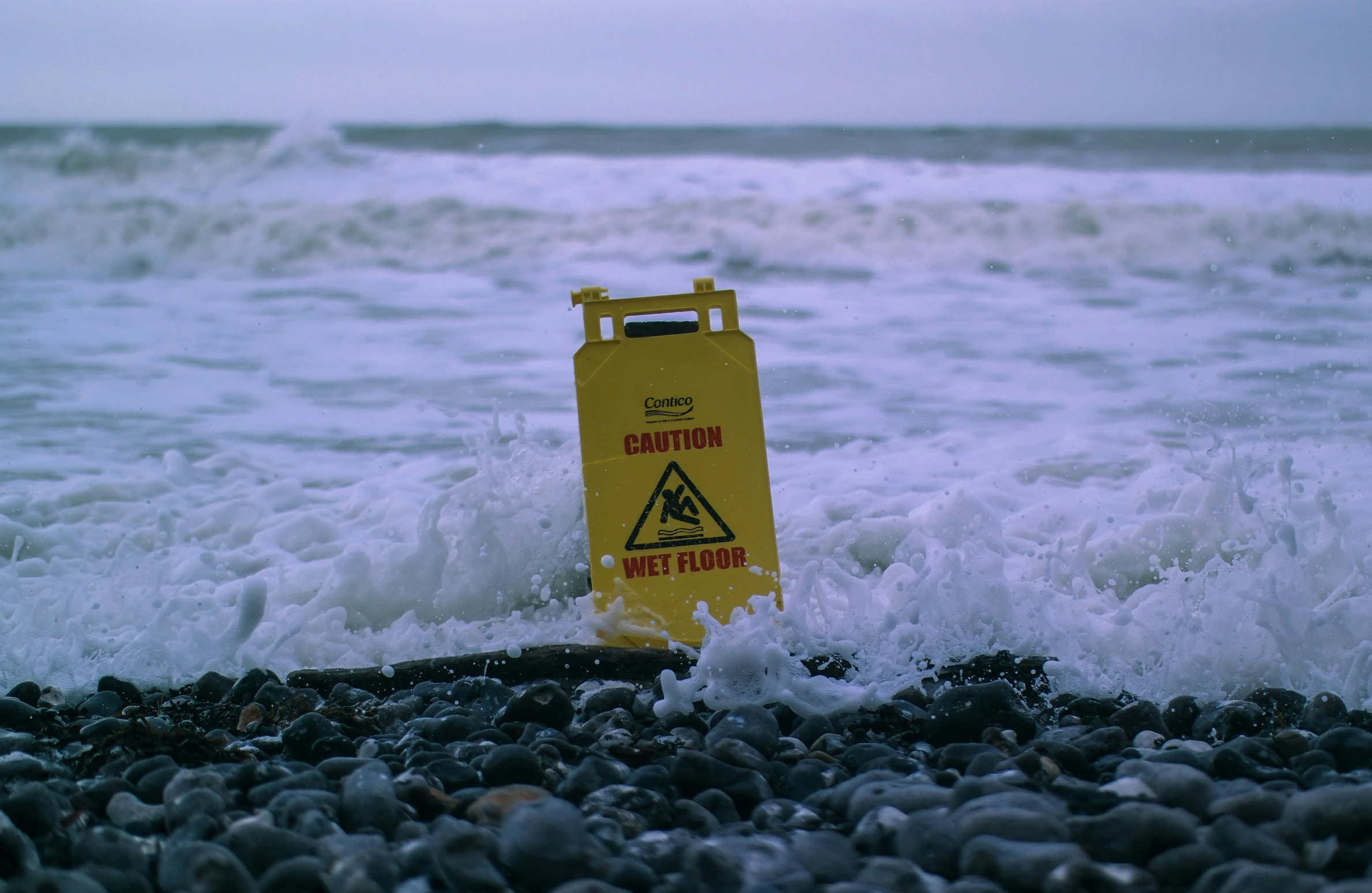 a yellow caution sign sitting on top of rocks next to the ocean