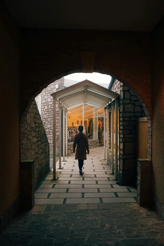 woman in black coat walking through tunnel with stone walkway