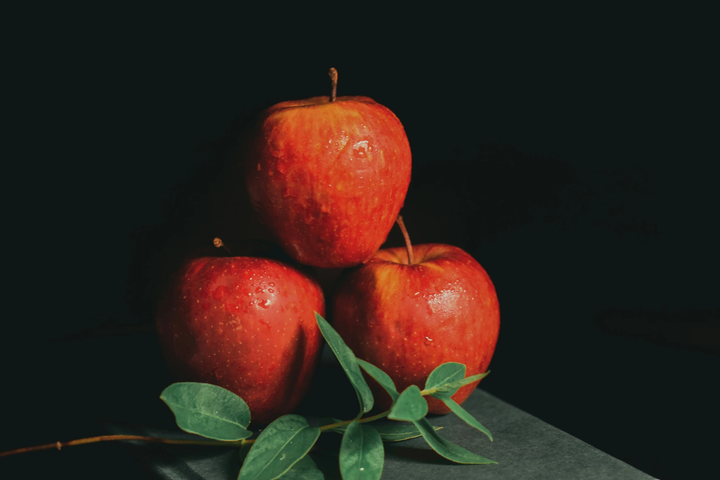 three apples with green leaves on top of a table