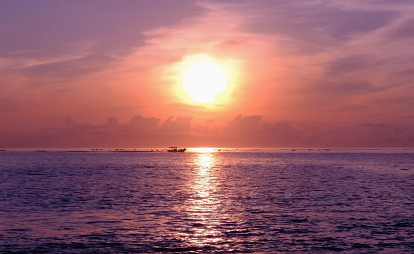 a small ship is coming toward shore with the sun setting