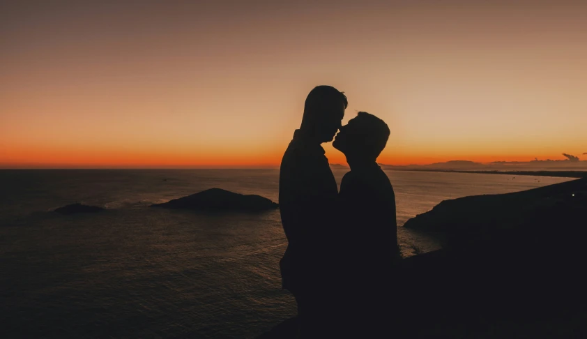 two people are kissing while standing in front of a sunset