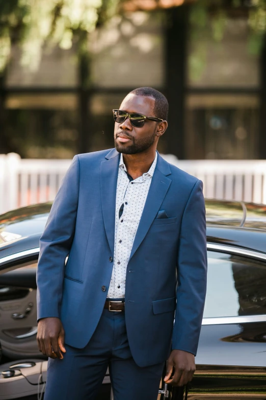 an african american man wearing sunglasses is standing by a black car