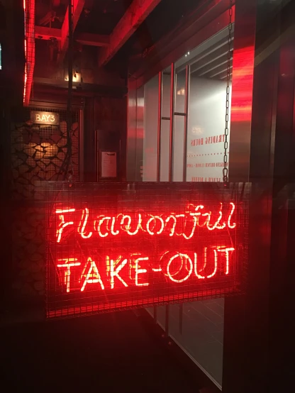 a lighted sign reading flavous, take out sits on the floor of a bar