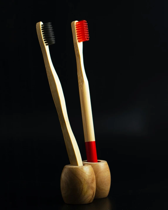 two toothbrushes sit in a wooden cup with toothpaste on it