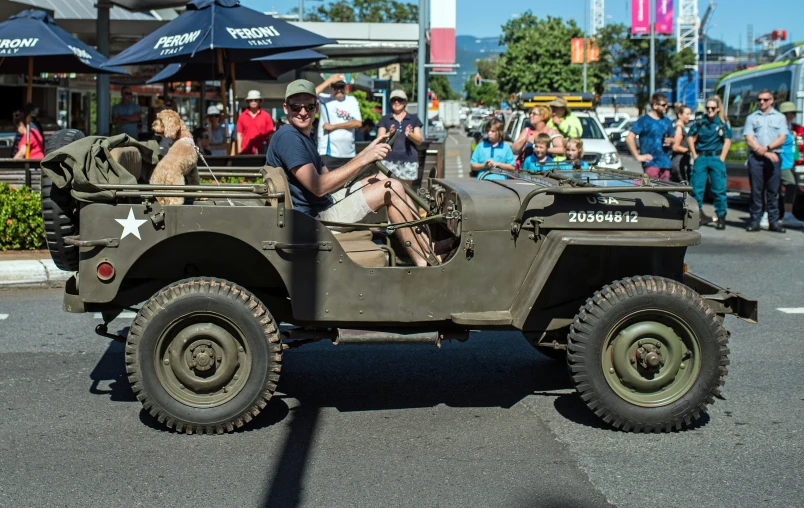 a military jeep in the parade with people sitting and walking