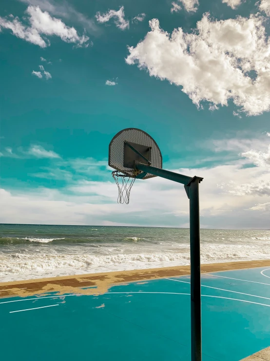 an empty blue basketball court on the beach with a sky background