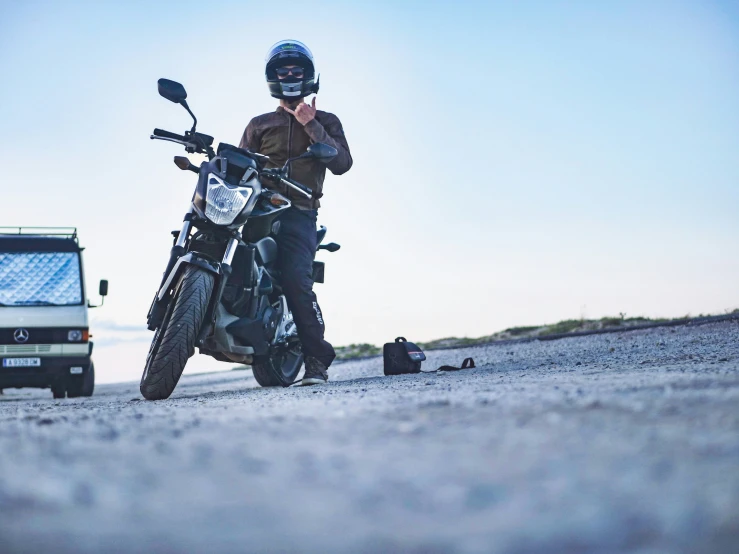 a motorcyclist standing next to his parked bike on the road