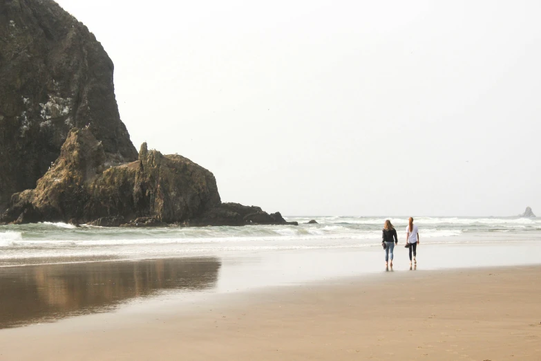 two people are walking along the beach