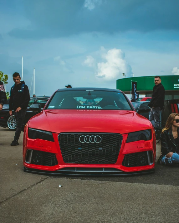 people sitting next to a red sports car