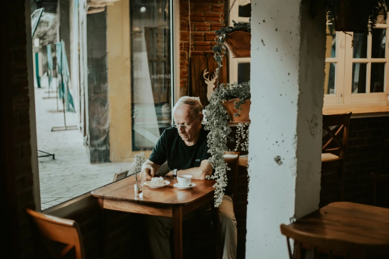 an older man sitting at a wooden table in front of a window