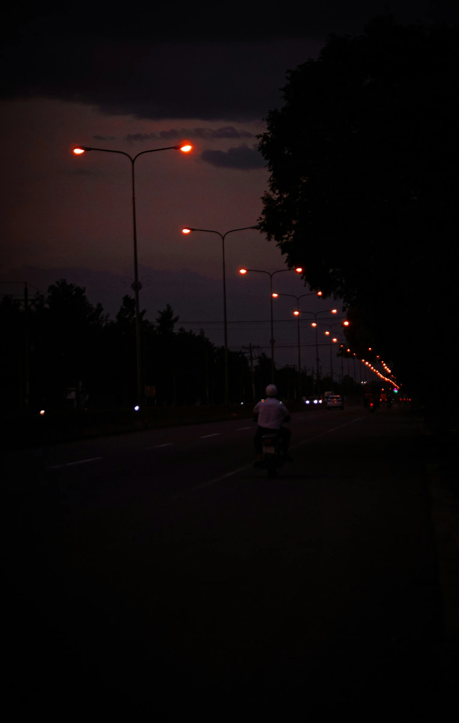 a dark night is lit by street lights and a man on his motorcycle