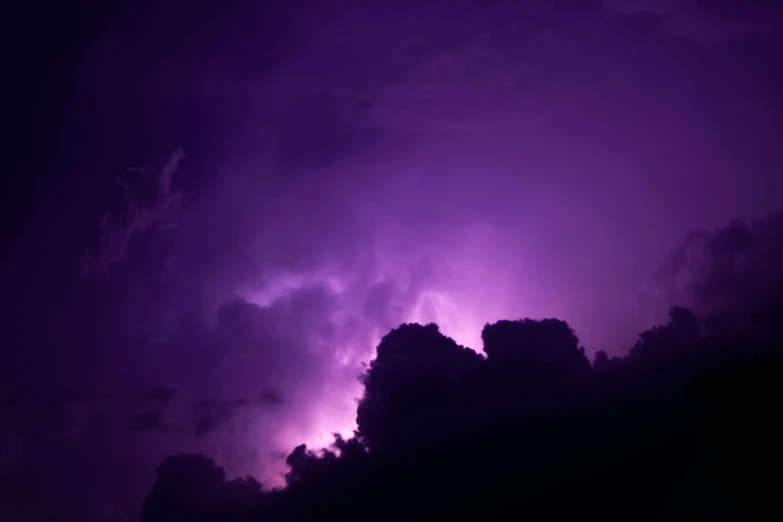 a very dark purple cloud with bright lightening behind it
