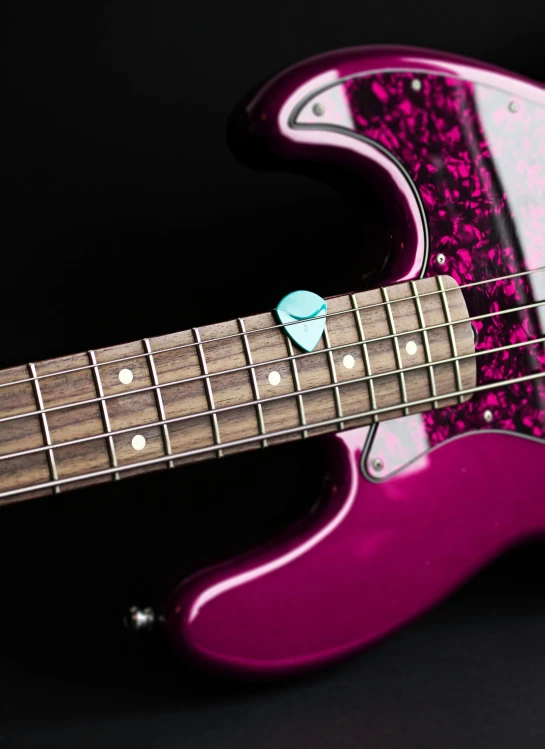 a close up s of a pink electric bass guitar with a red and white swirl pattern