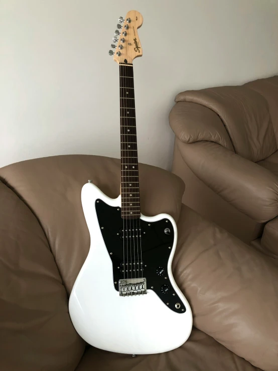 white and black guitar lying on a brown leather sofa